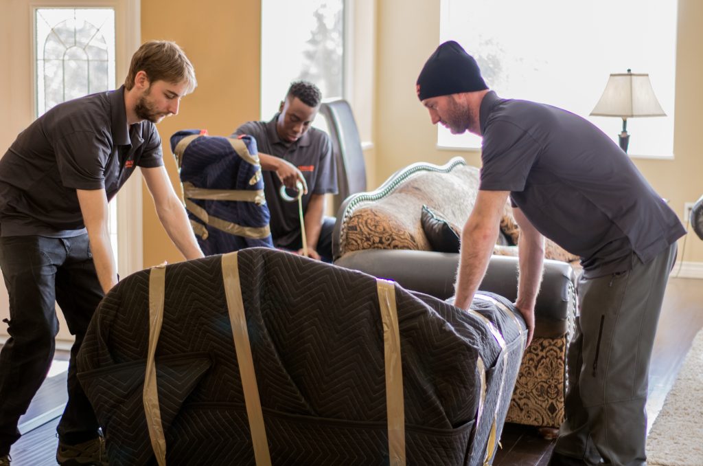Three full-service movers wrapping furniture during a residential move.