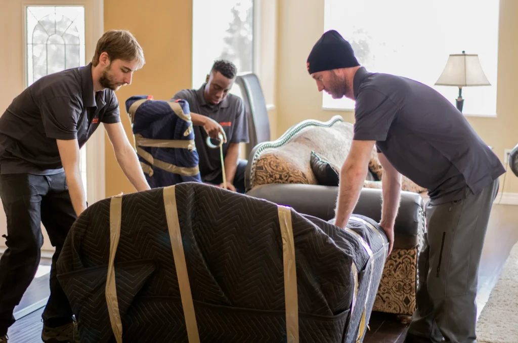 Three professional movers wrapping furniture during a residential move.