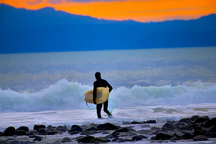 A man in wet suit carrying a surf board walking out to the ocean.