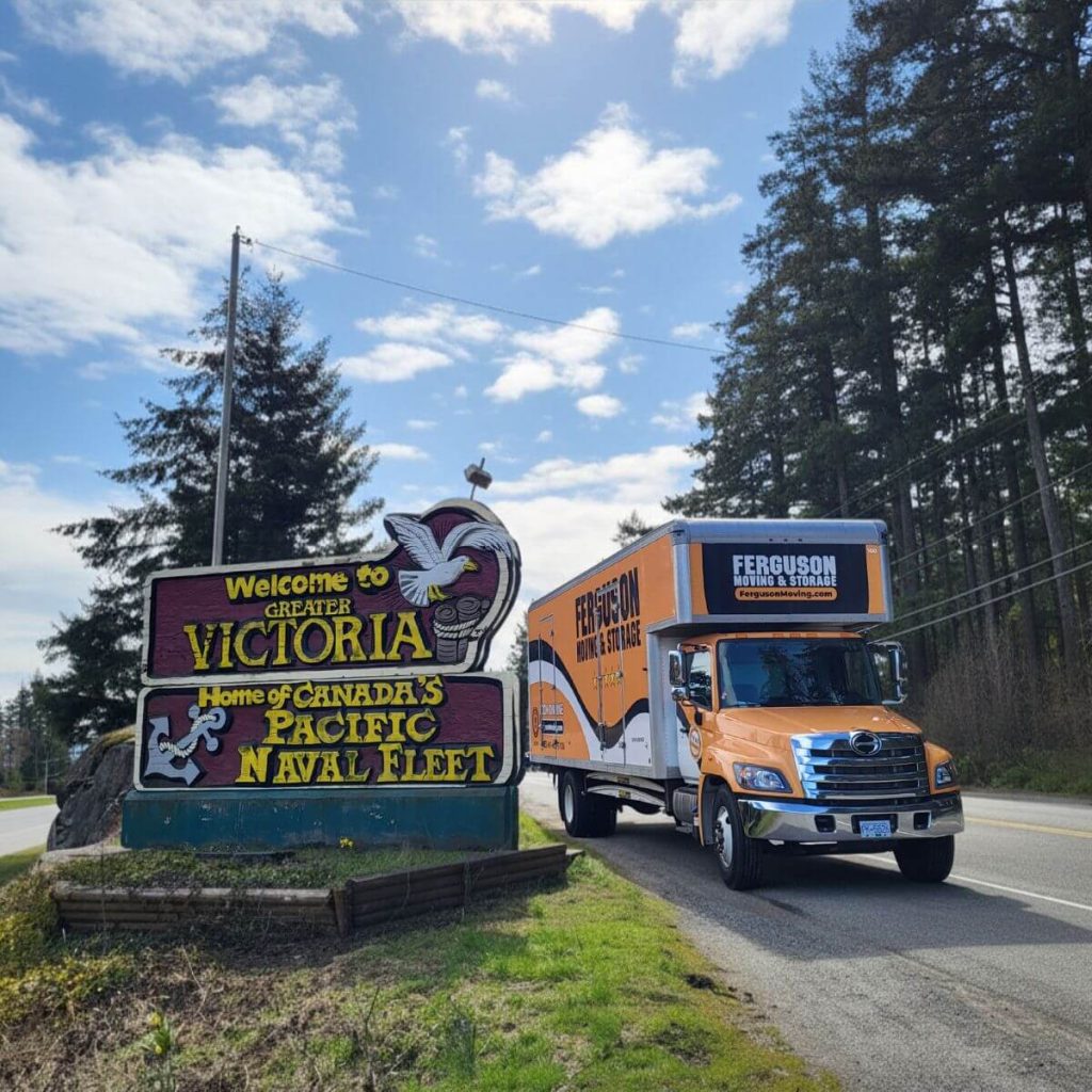 Moving truck driving by a Welcome to Greater Victoria sign.