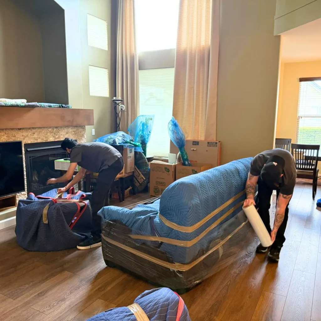 Two Ferguson movers wrapping furniture in a living room.