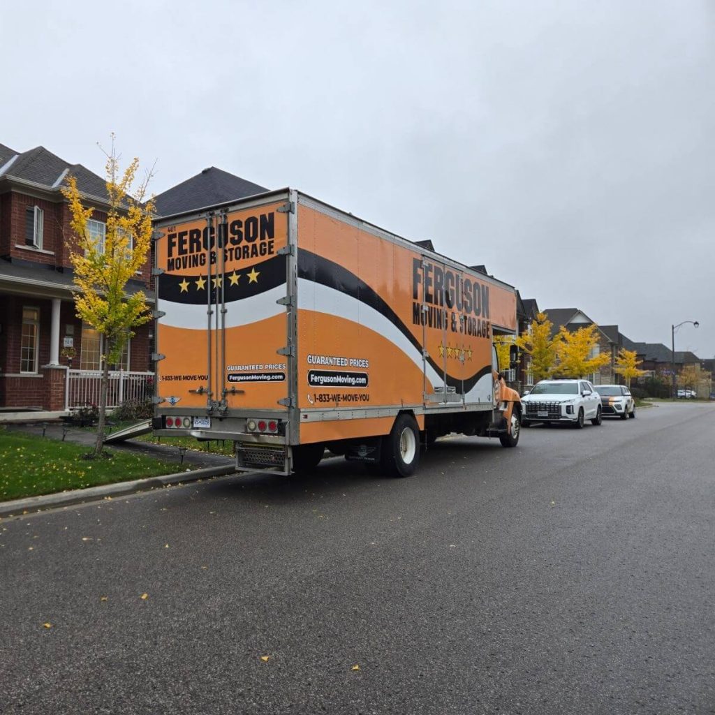 Back of the moving truck showing its five-star branding, parked beside a golden maple sapling on a cloudy fall day
