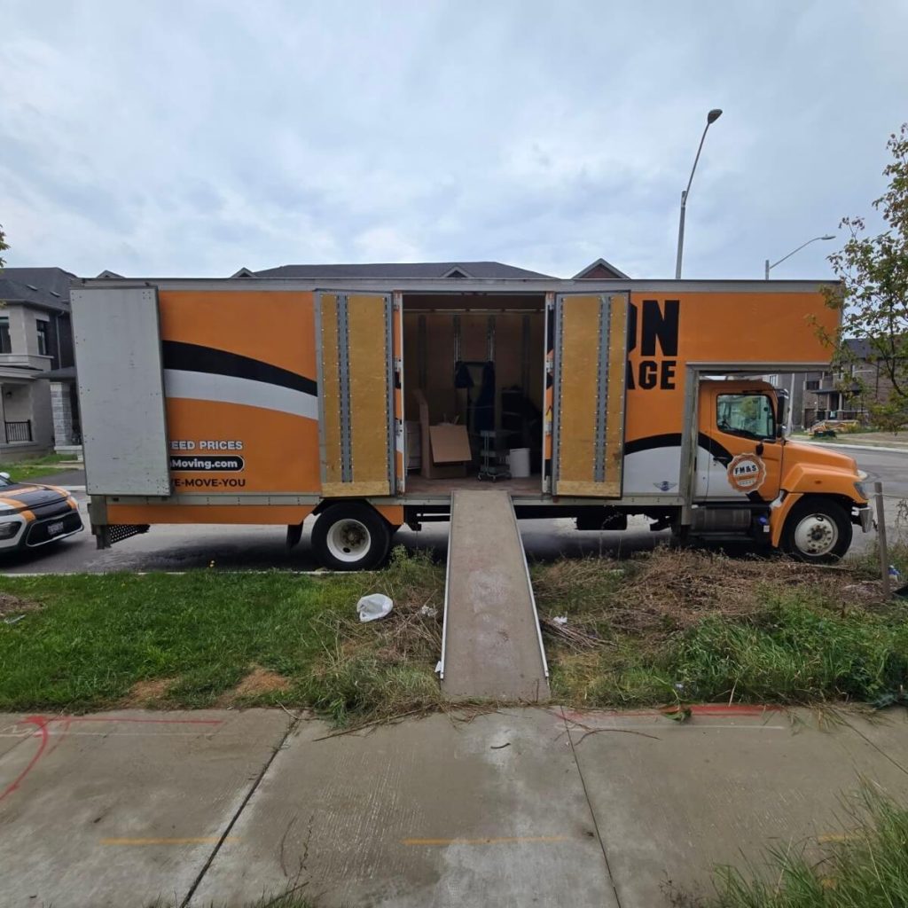 Side doors of the truck swung open with a ramp running down to the sidewalk, showing furniture partly loaded inside